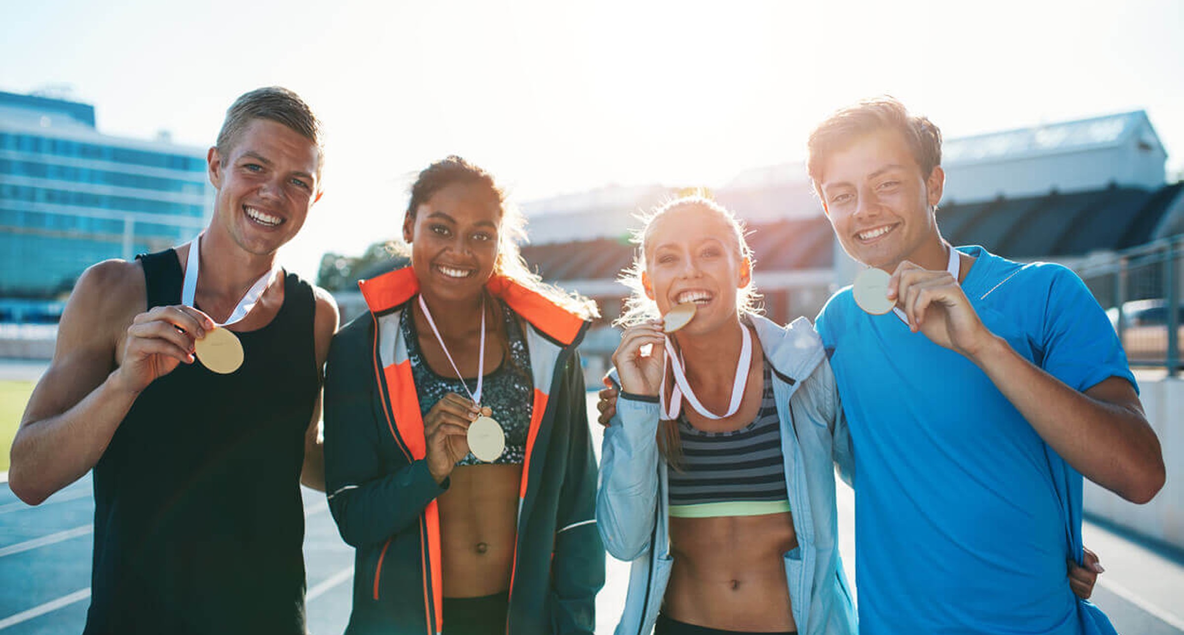 Four smiling athletes holding gold medals on a sports track